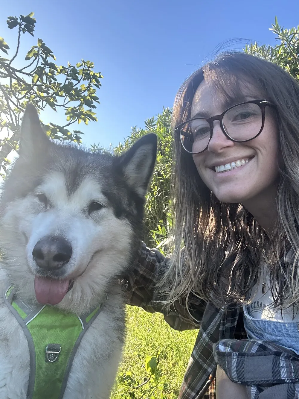 Charlotte smiling outdoors with her dog beside her, with trees and blue sky behind.